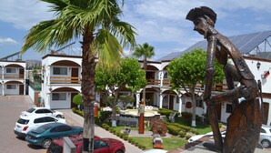 A hotel with multiple-story buildings, a parking area with several cars, and a central garden with a statue.
