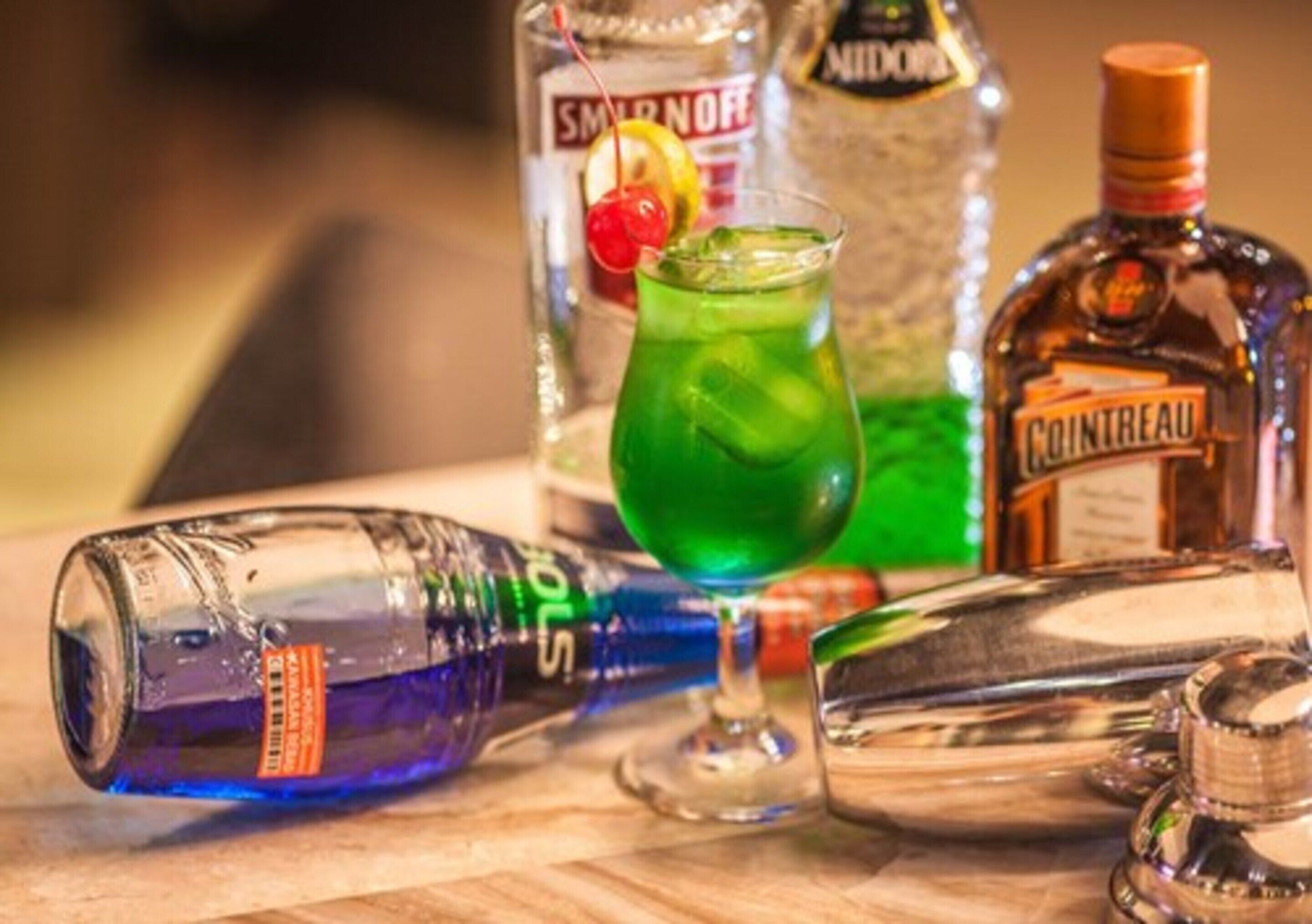 A bottle of Cointreau, a bottle of Smirnoff, and a glass with a green drink on a wooden surface.