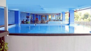 A large indoor swimming pool with a clear view of the pool area, a seating area, and a covered section with tables and chairs. - King's Hotel Nagoya Batam (Batam)
