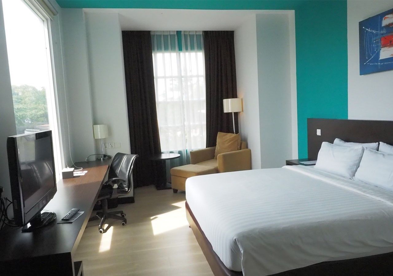 A hotel room with a bed, desk, chair, TV, and a window with curtains.