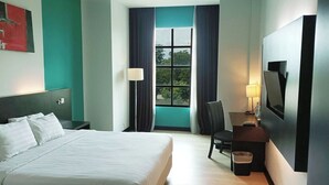 A hotel room with a bed, a desk with a chair, a TV, and a window with curtains. - King's Hotel Nagoya Batam (Batam)