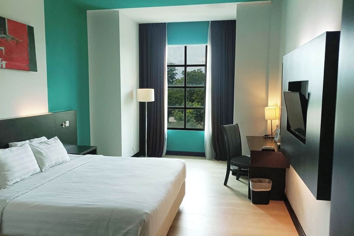 A hotel room with a bed, a desk with a chair, a TV, and a window with curtains.
