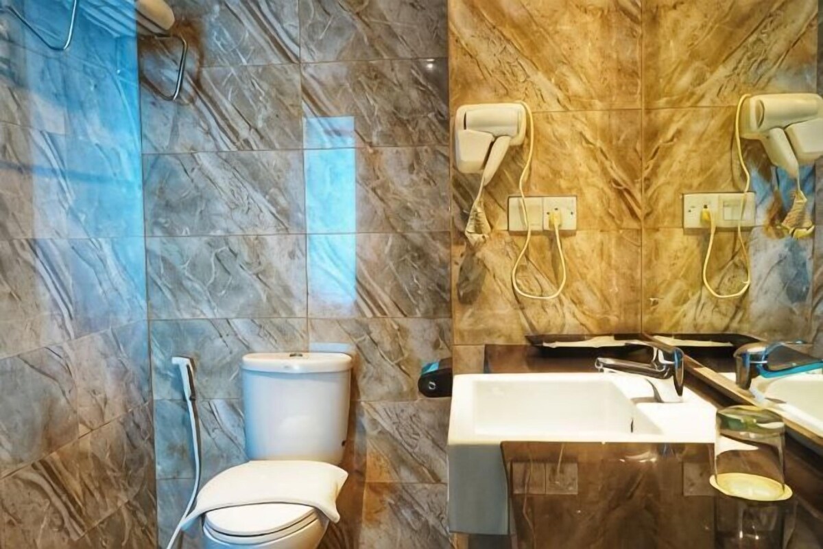A bathroom with a marble wall, a toilet, a sink, and a mirror with a hairdryer.
