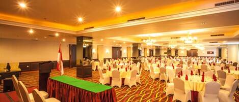 A banquet hall with rows of round tables, white chairs, and a red carpeted floor.