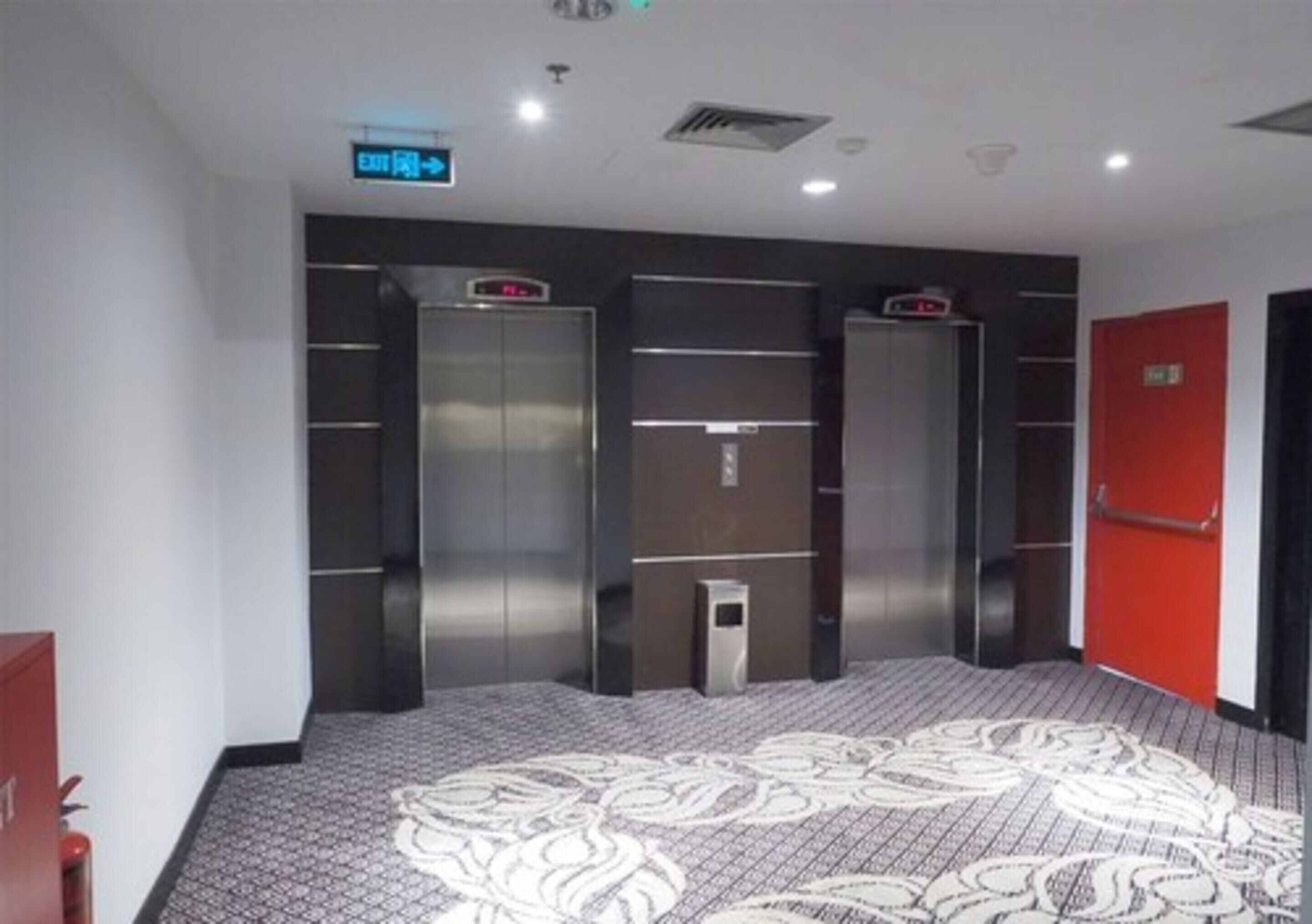 A hotel lobby with a patterned carpet, a red door, and three elevators.