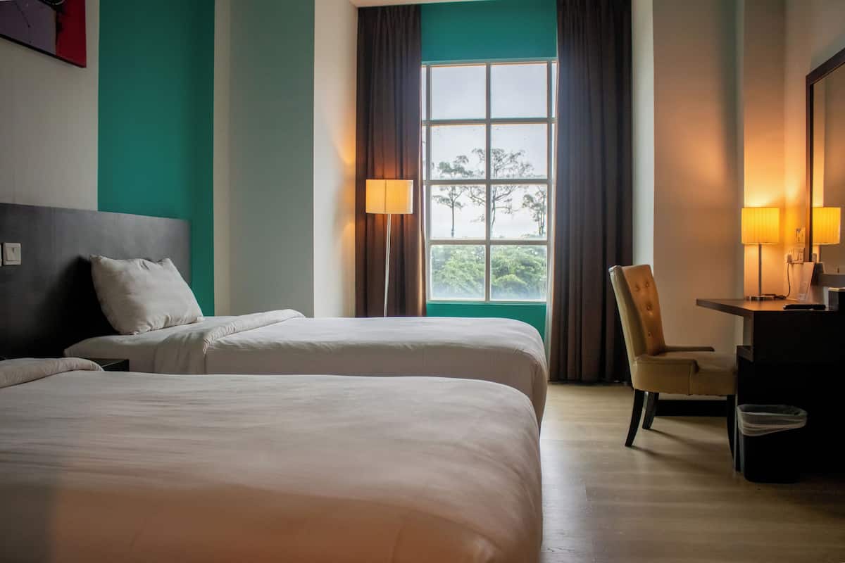 A hotel room with two beds, a desk, a chair, and a window with curtains.