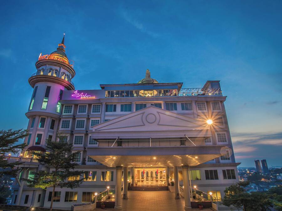 Un hotel elegante con una torre destacada, un acceso amplio y vistas de la ciudad al fondo.