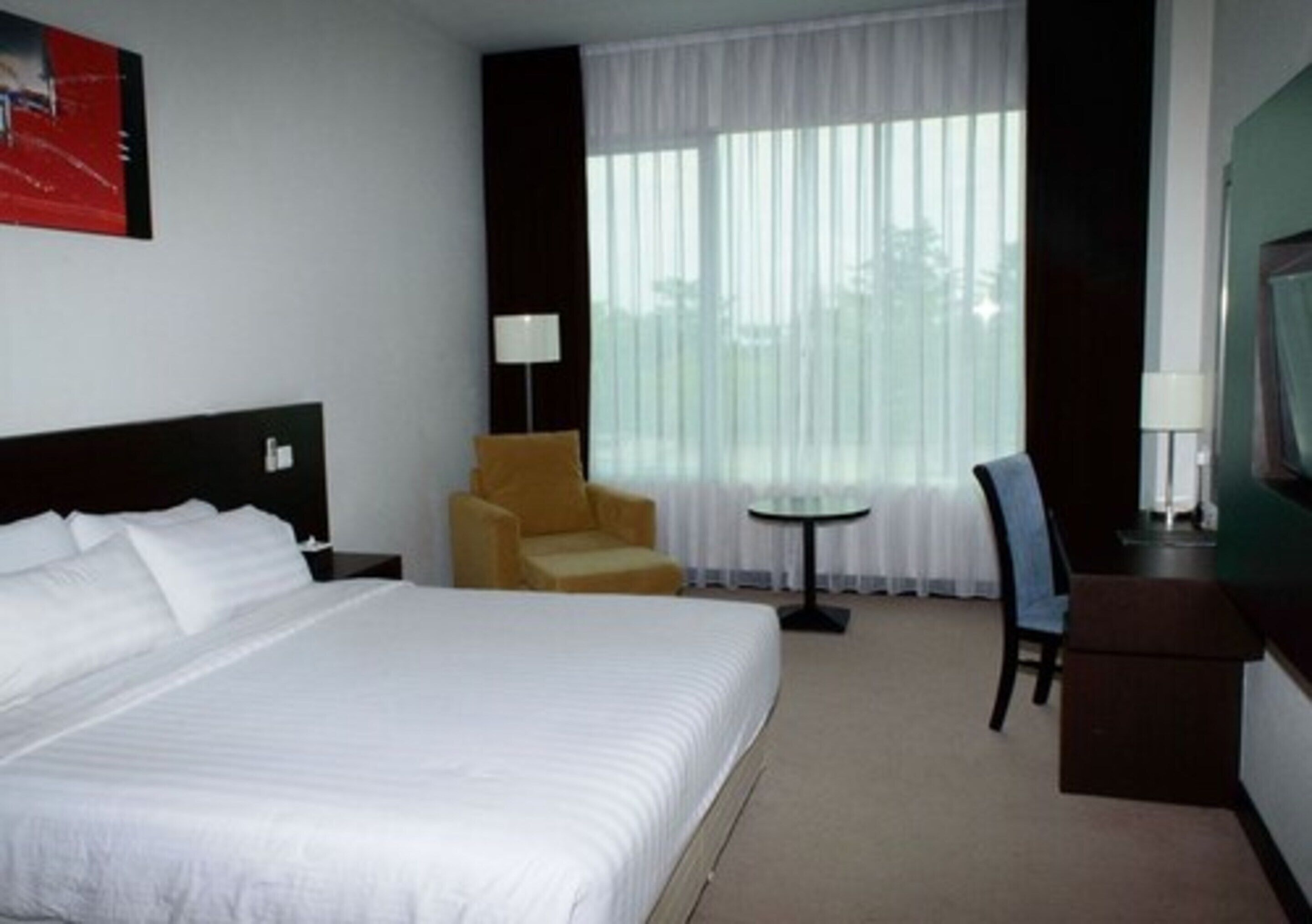 Une chambre d’hôtel avec un grand lit, une petite table ronde, une chaise et un bureau avec une lampe.