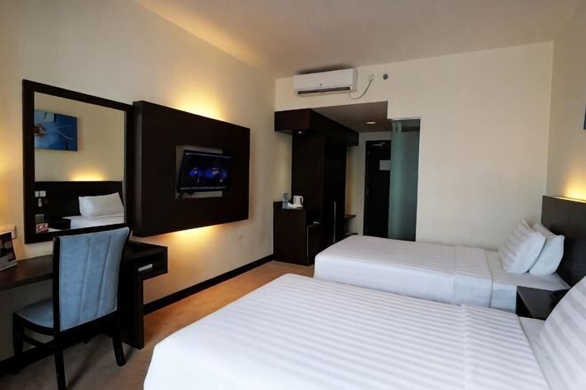 A hotel room with two beds, a desk, a chair, a TV, and an air conditioning unit.