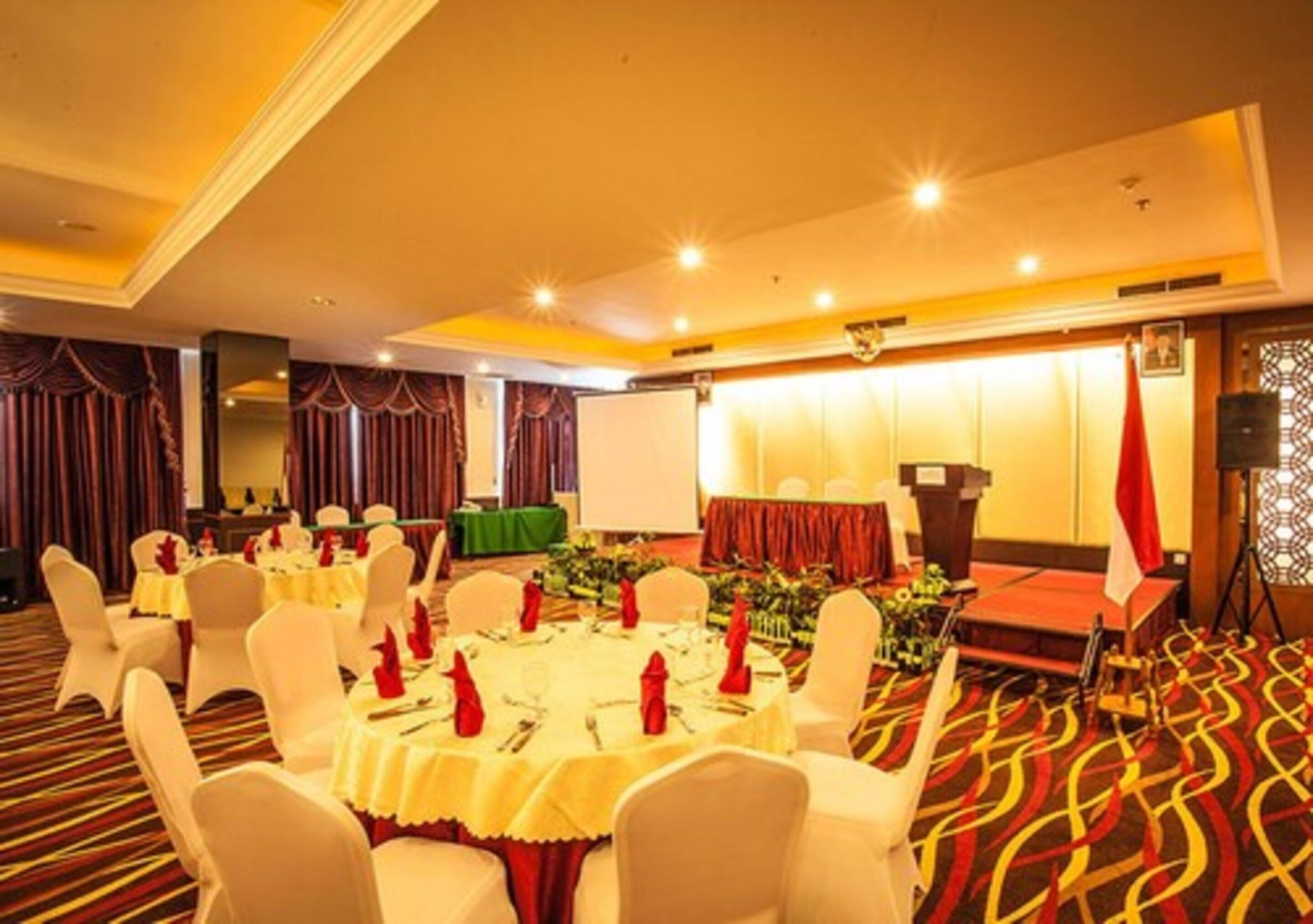 A banquet hall with round tables set for dining, a stage with a podium, and a patterned carpet.