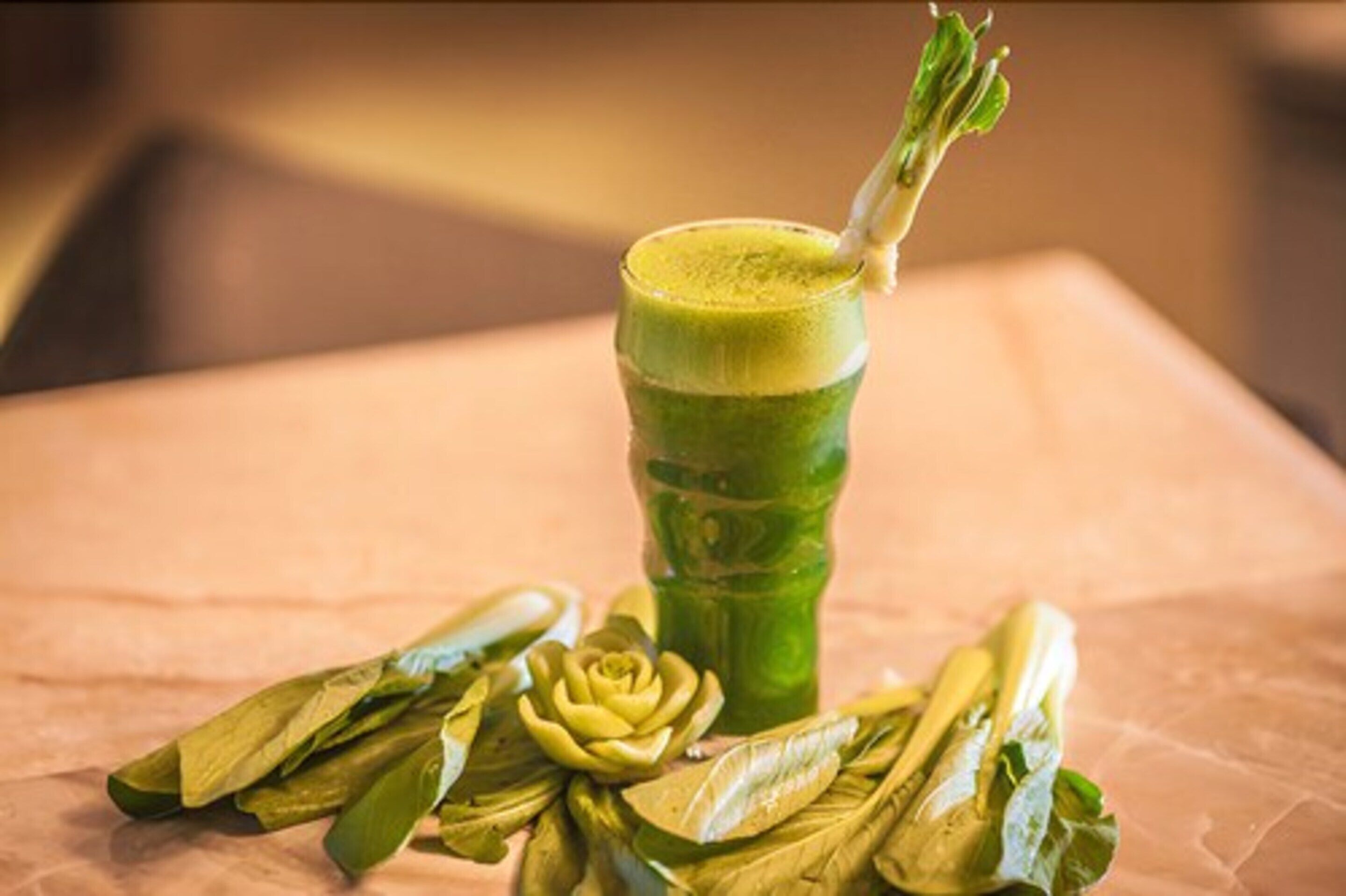 A glass of green drink with a garnish on a table with a pink tablecloth.