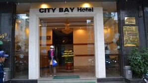La entrada del Hotel City Bay, con un letrero visible, un recibimiento agradable y una planta en maceta.