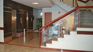 Un interior moderno con una escalera de cristal, un letrero de salida visible y una planta en maceta.