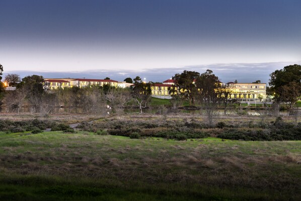 A large hotel with multiple buildings, a grassy field in the foreground, and a body of water behind the hotel.