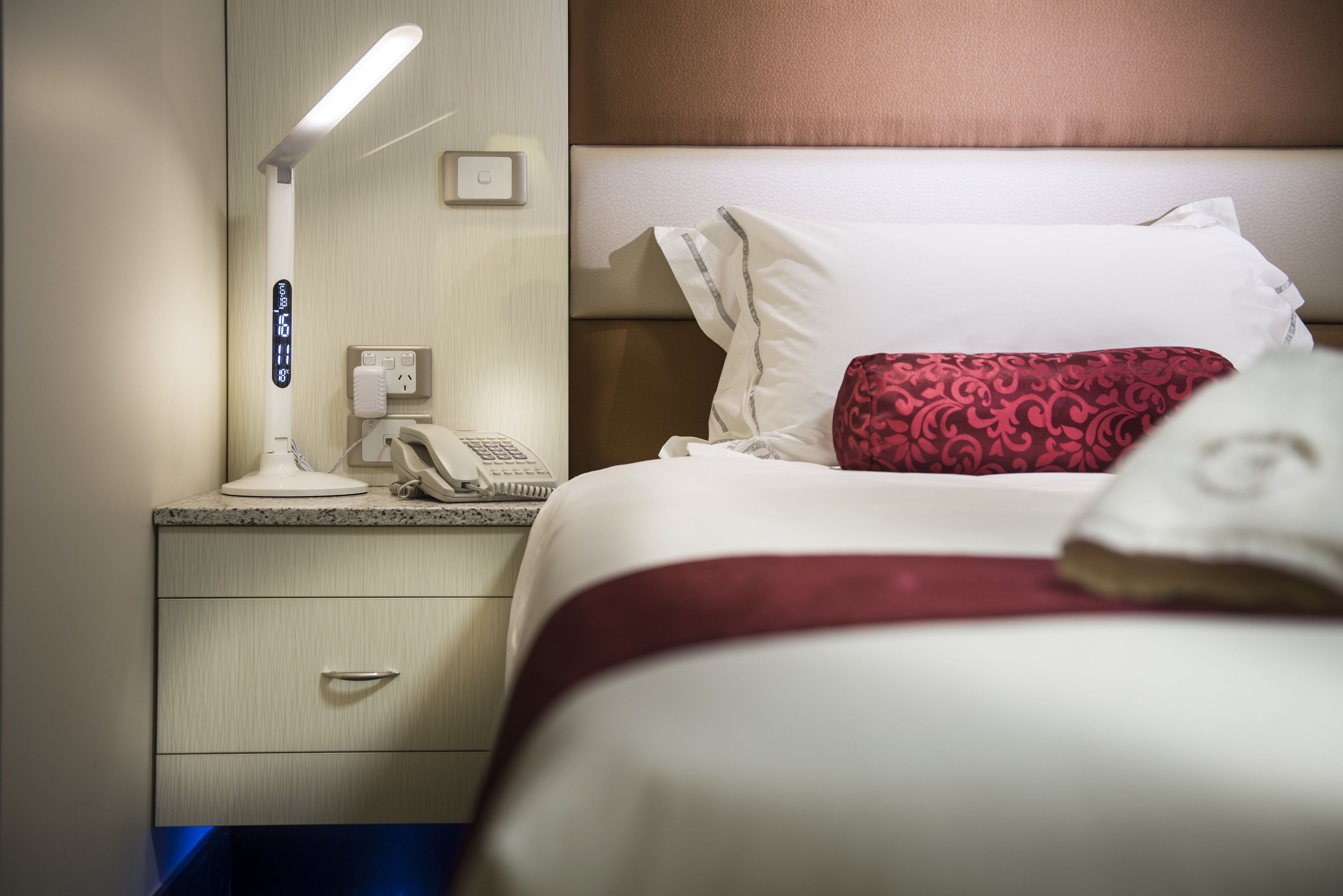A hotel room with a bed, a bedside table with a lamp, a phone, and a drawer.