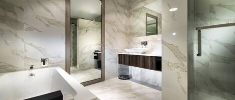 Un baño moderno con una bañera grande, una ducha con mampara de vidrio y un tocador con encimera de mármol.