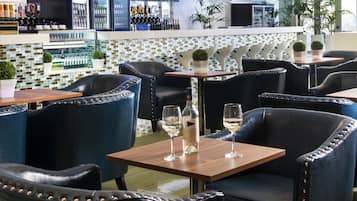 Un'area bar moderna con poltrone e tavoli in pelle, una parete rivestita in piastrelle e un lampadario.