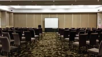 A conference room with rows of chairs facing a white projection screen, carpeted floor, and a neutral color scheme.