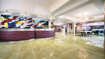 A lobby with a marble floor, a tufted reception desk, a colorful abstract wall, and a chandelier.
