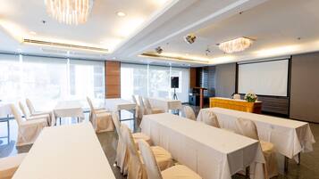A conference room with tables and chairs, a podium, a projector screen, and a large window.