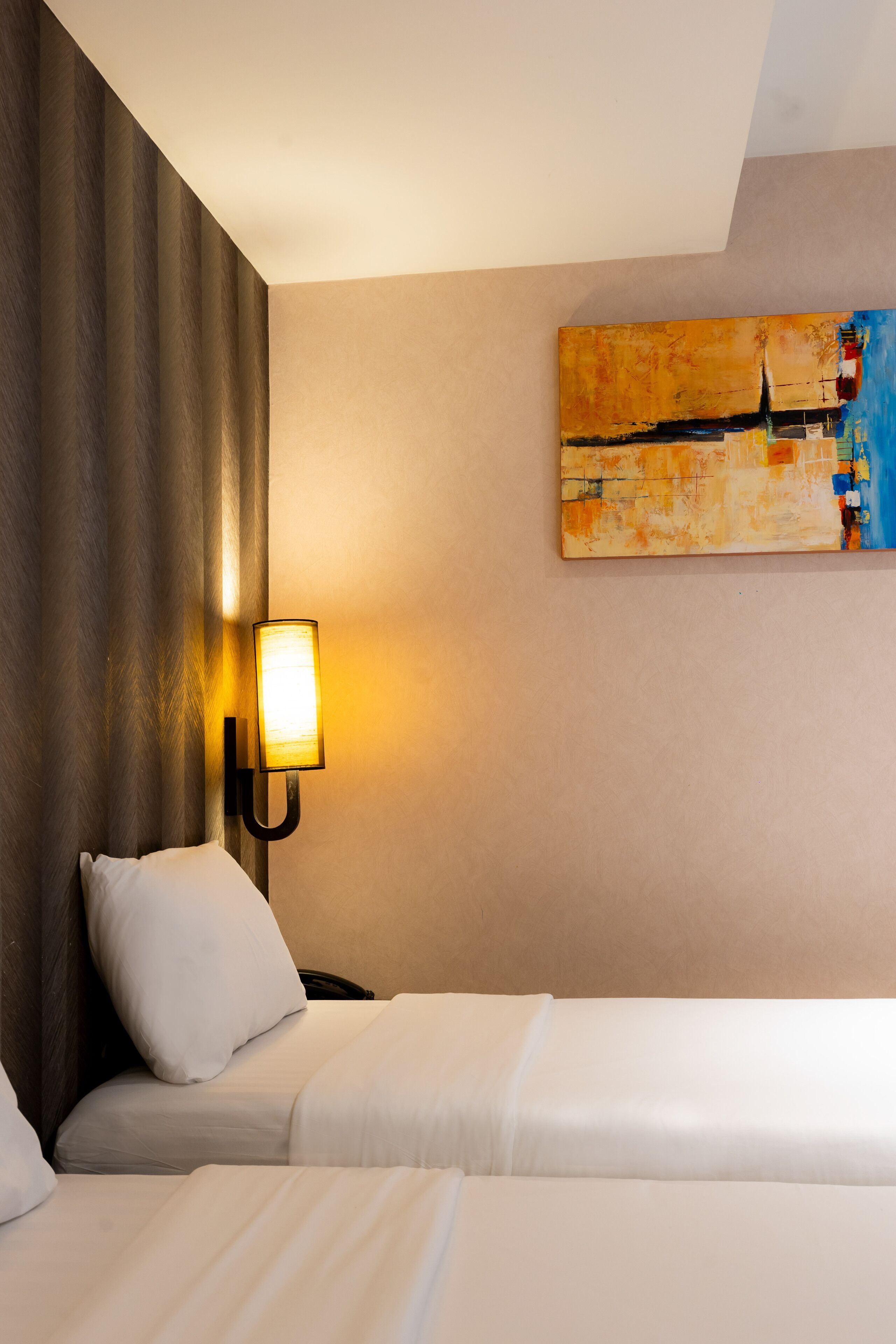 Habitació d'hotel amb dos llits, un quadre a la paret i una làmpada penjada a la paret.