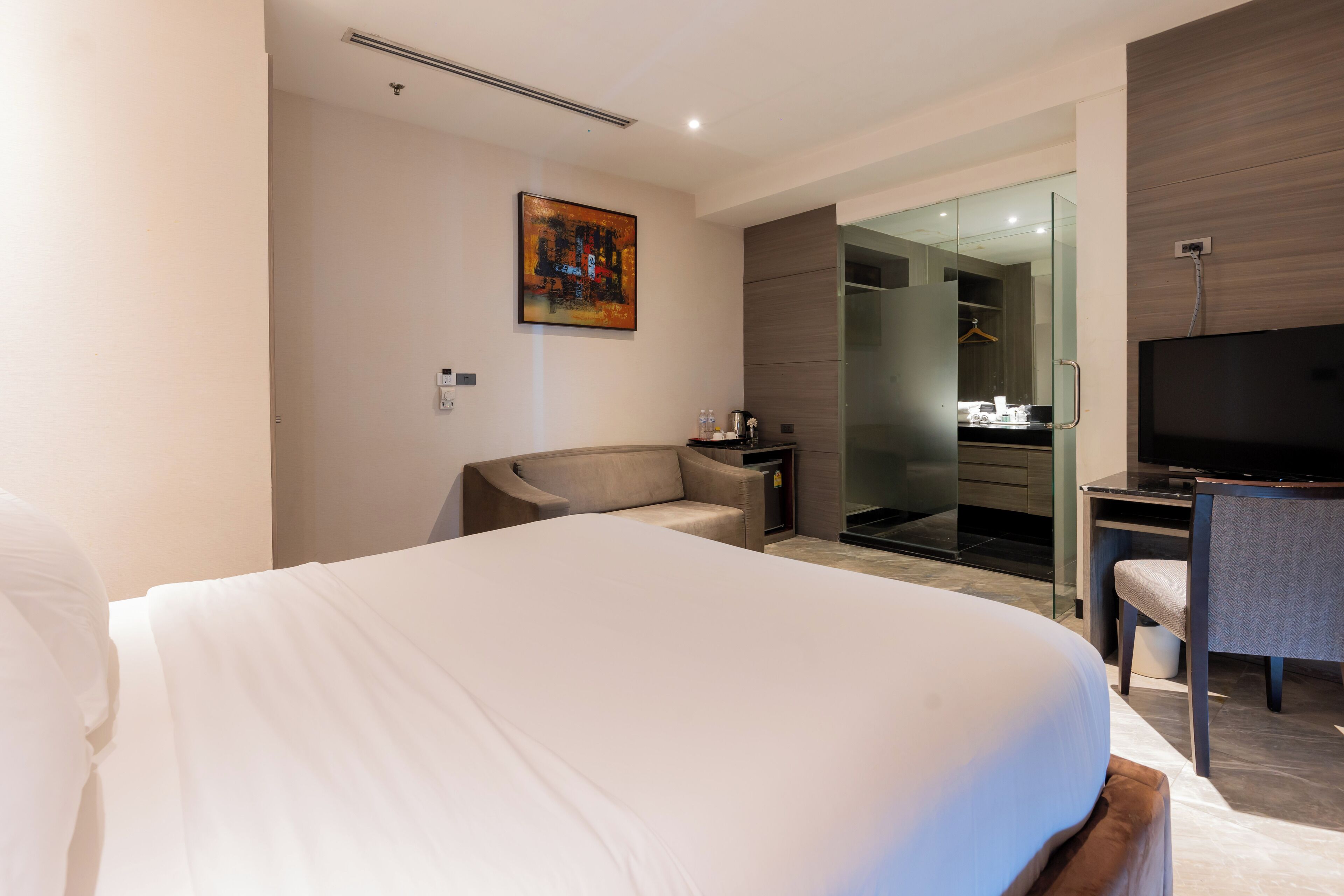 A modern hotel room with a large bed, a desk with a chair, a television, and a walk-in closet with a mirror.