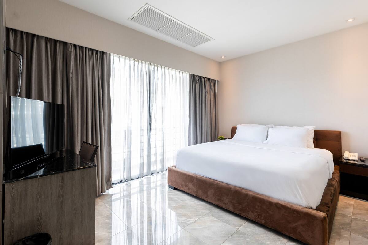 A modern hotel room with a large bed, a flat-screen TV, and a desk with a laptop.