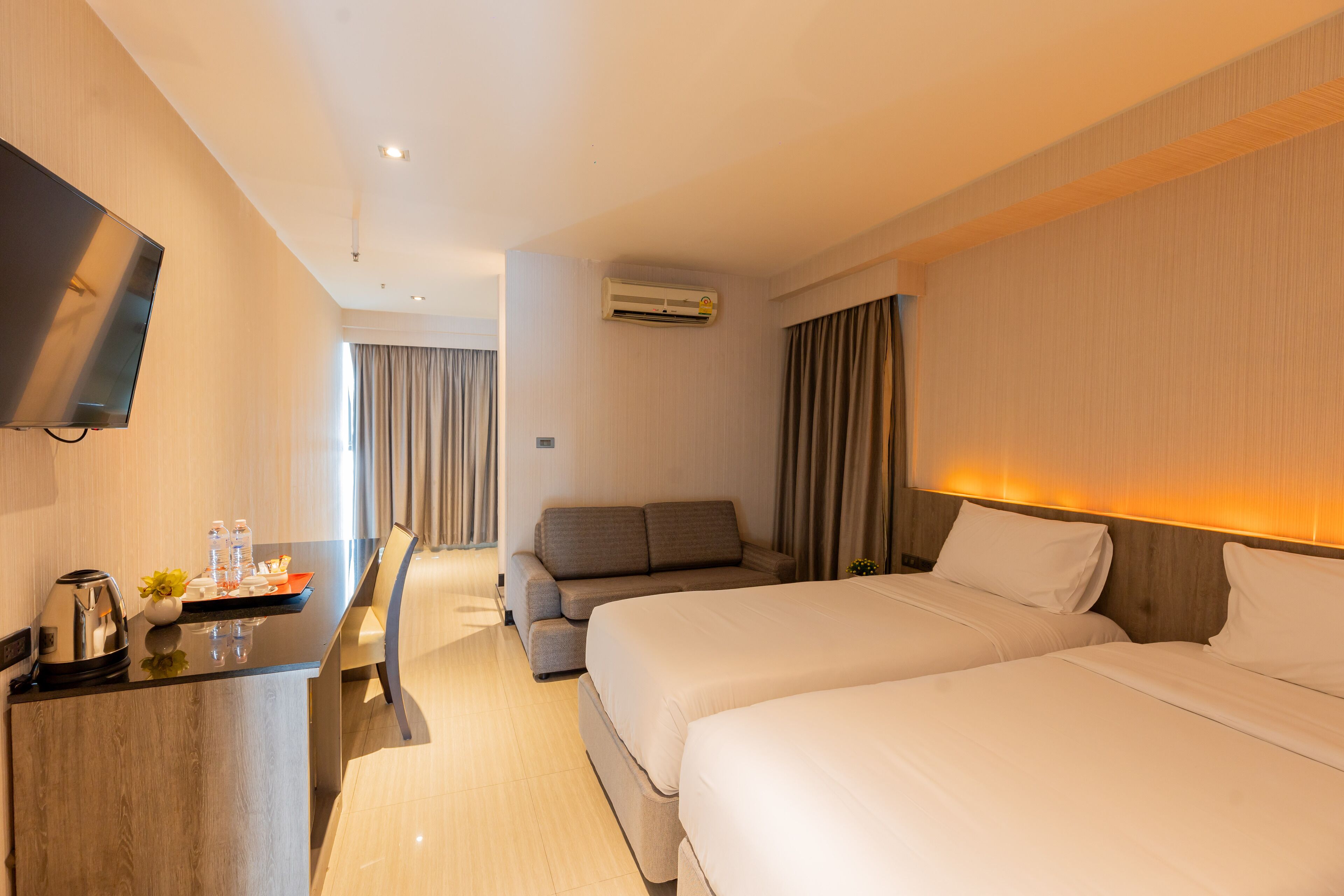 A hotel room with two beds, a desk with a coffee maker, a TV, and an air conditioning unit.