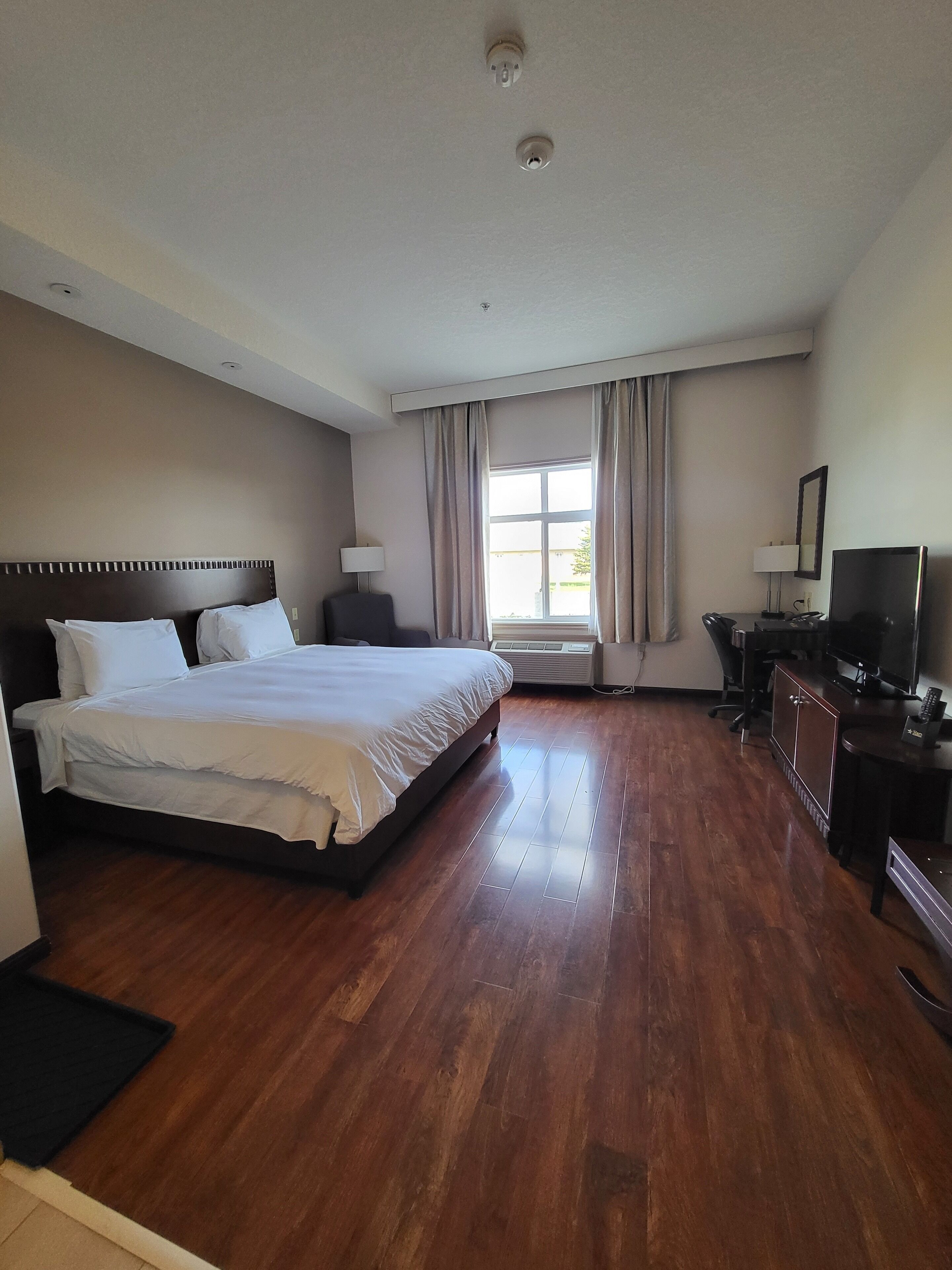 A hotel room with a large bed, a desk with a computer, a TV, and a window with curtains.