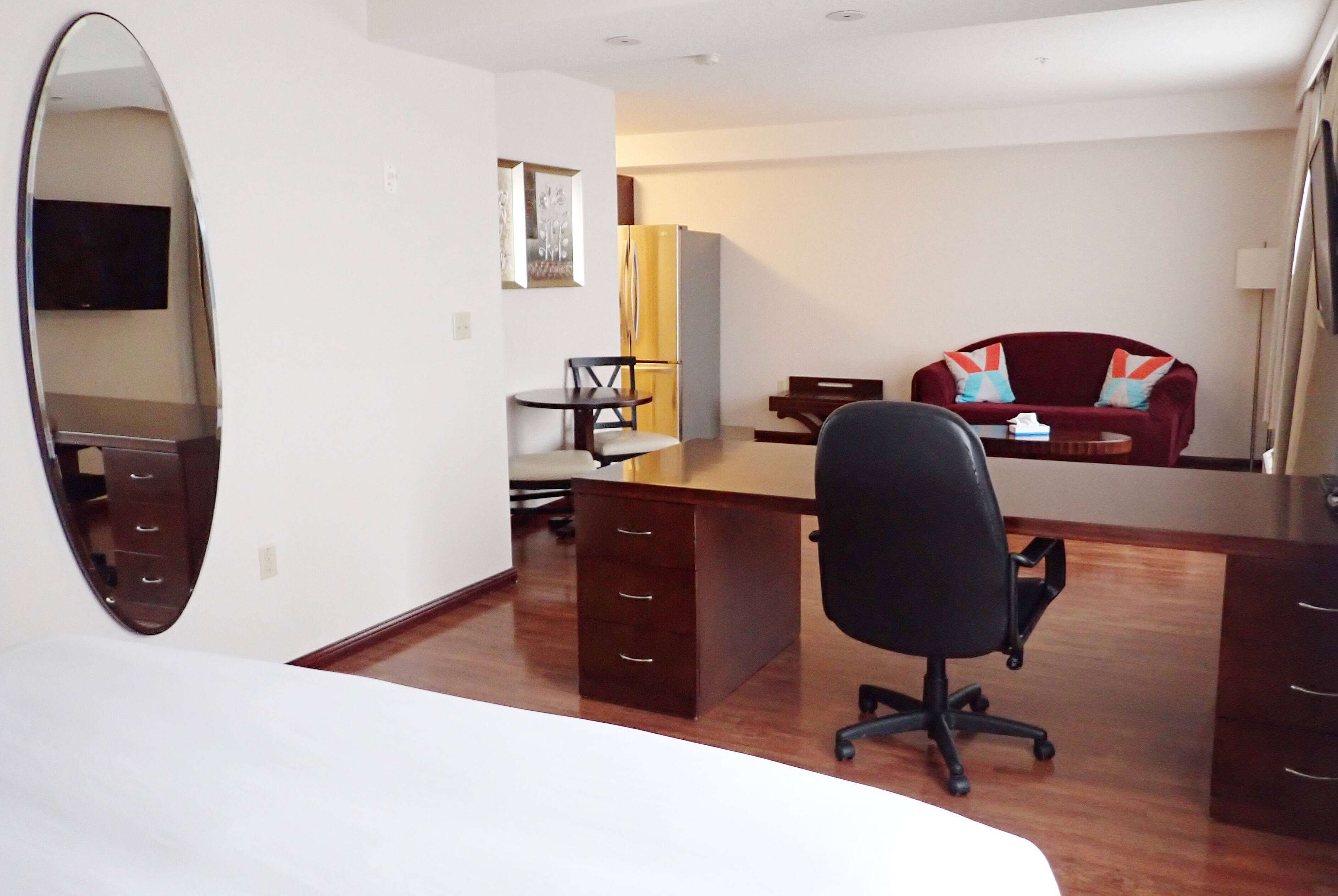 Una habitación de hotel con una cama grande, un escritorio con una silla, un armario, un espejo, un televisor y un sillón rojo.