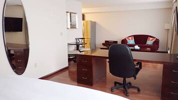 Una habitación de hotel con una cama grande, un escritorio con una silla, un armario, un espejo, un televisor y un sillón rojo.
