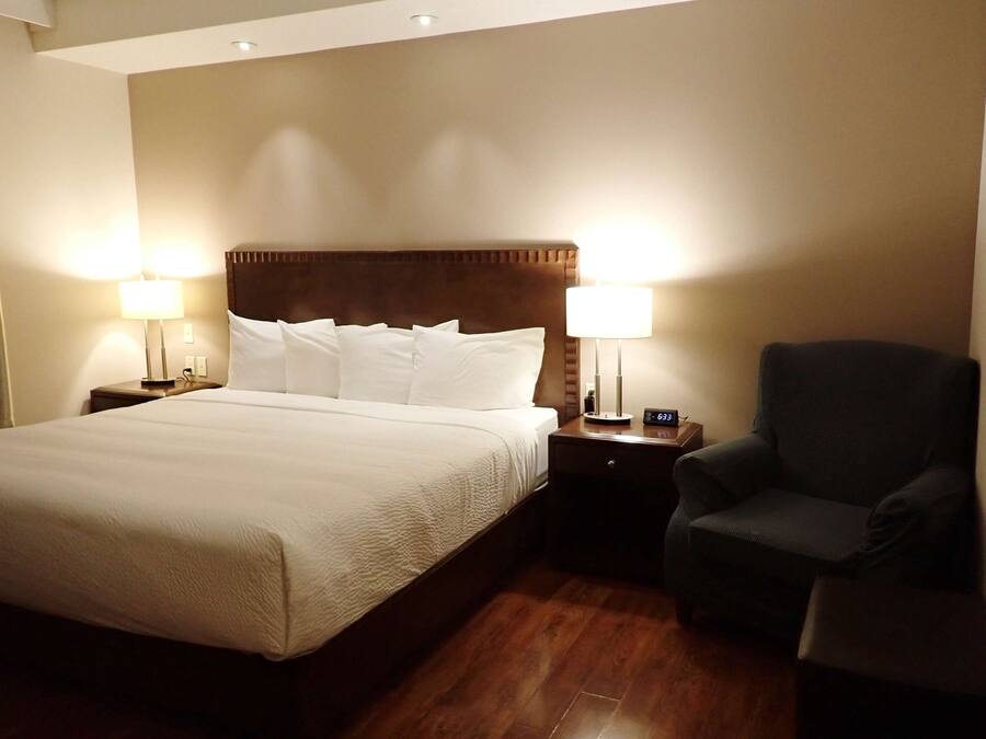 A hotel room with a large bed, two bedside lamps, a chair, and a nightstand with a clock.