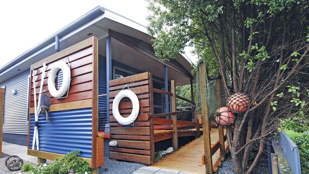 A modern house with a wooden deck, a small garden, and a blue exterior wall. - Strahan Bungalows (Strahan)
