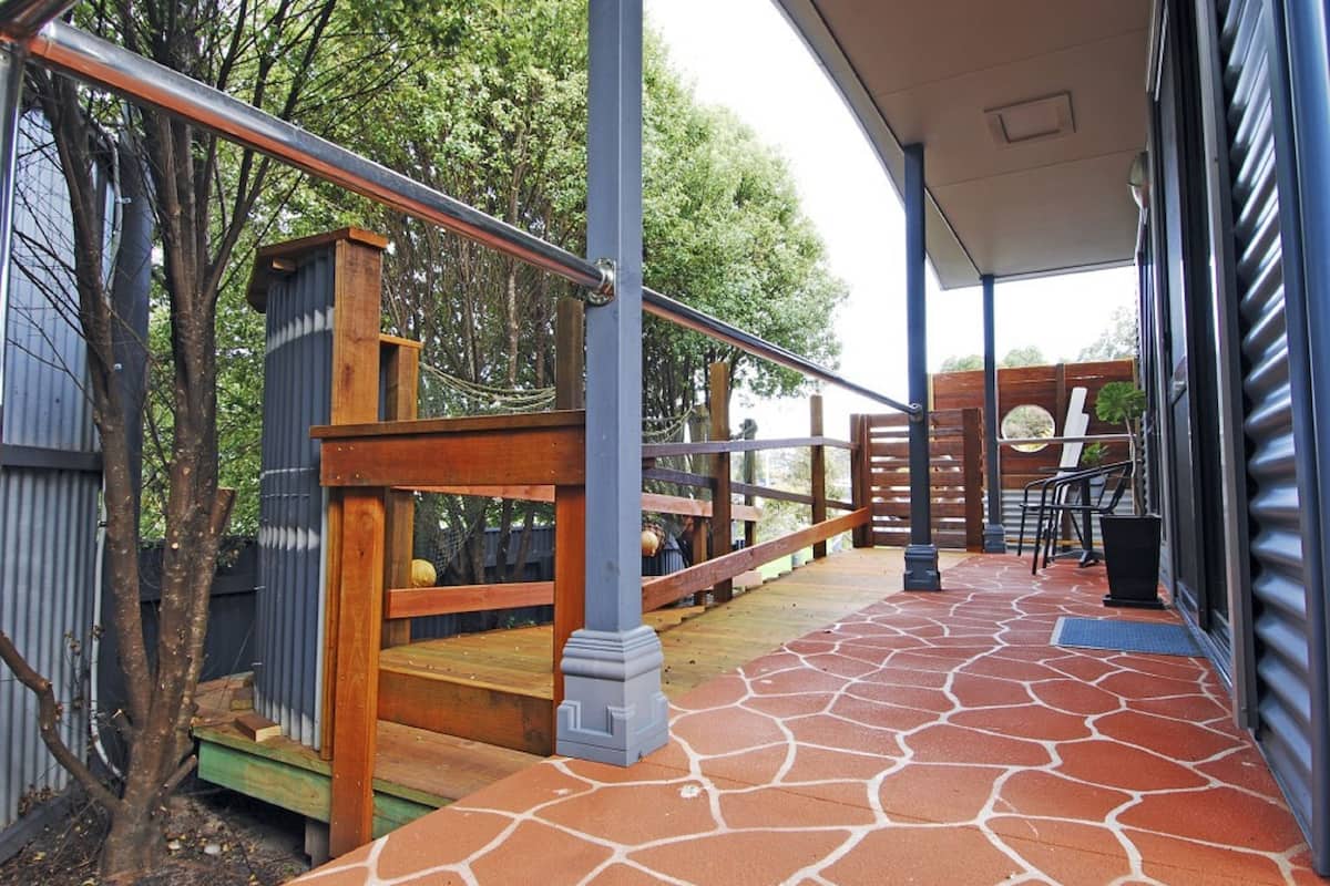 Un espacio al aire libre cubierto con una escalera de madera, barandilla metálica y piso de baldosas de piedra.