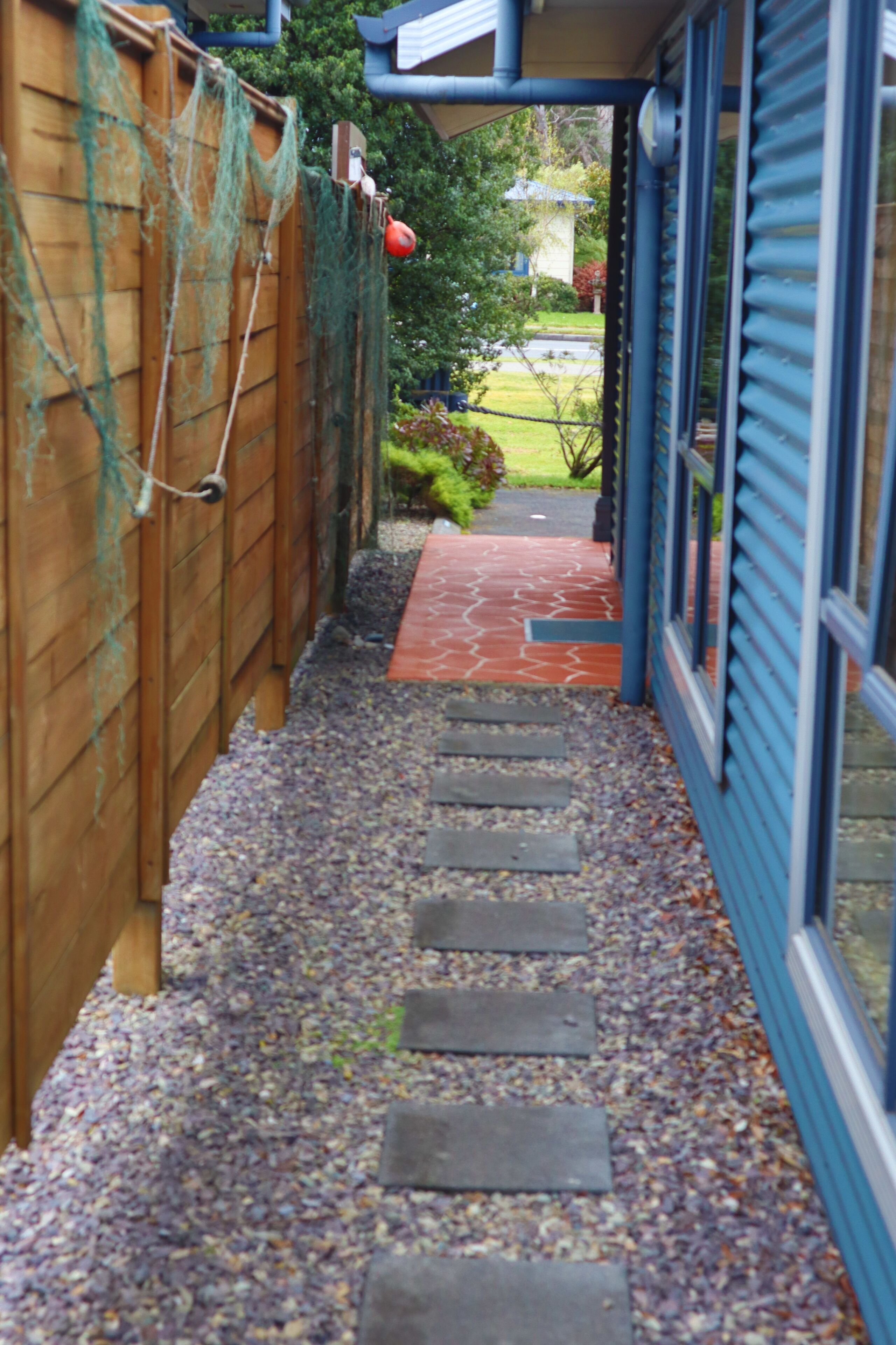 A narrow pathway with a wooden fence on one side and a blue building on the other.