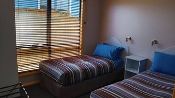 A bedroom with two beds, a nightstand, and a window with blinds.