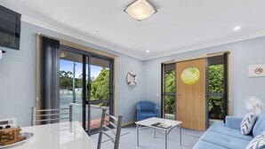 A modern room with a dining table, a blue sofa, and a chair. There is a large window and a door leading outside. - Strahan Bungalows (Strahan)