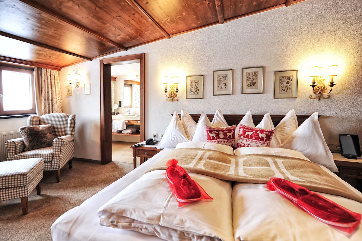 A hotel room with a large bed, checkered armchair, and a wooden ceiling.