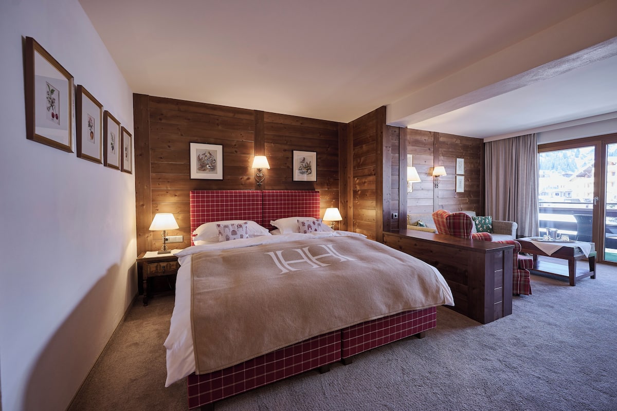 A hotel room with a large bed, wooden panel walls, a desk with a chair, and a view of the outside.