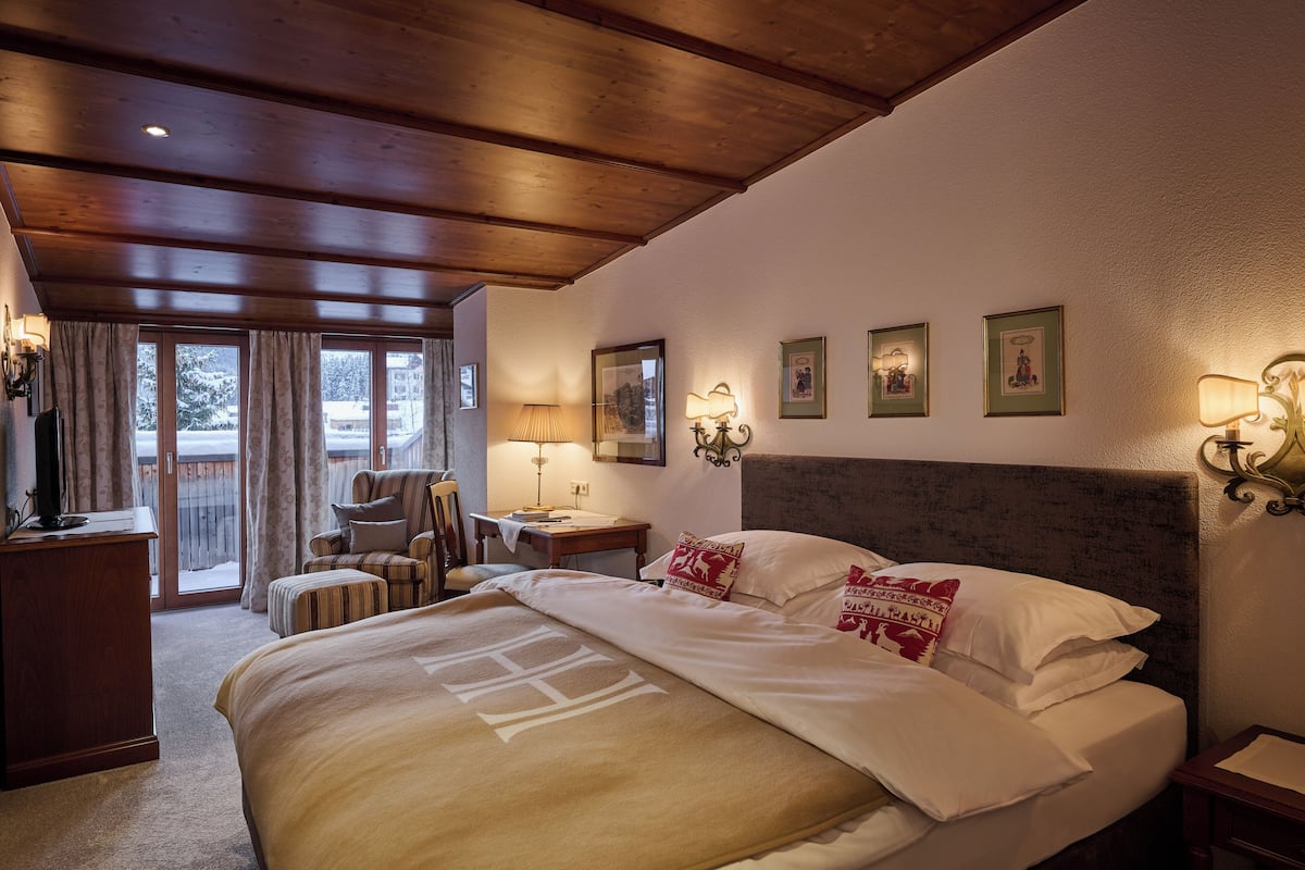 A hotel room with a large bed, a desk, a chair, and a view through a glass door.
