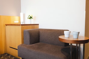 A corner seating area with a cushioned bench, a small round table with two white cups, a vase with flowers, and a wooden cabinet.