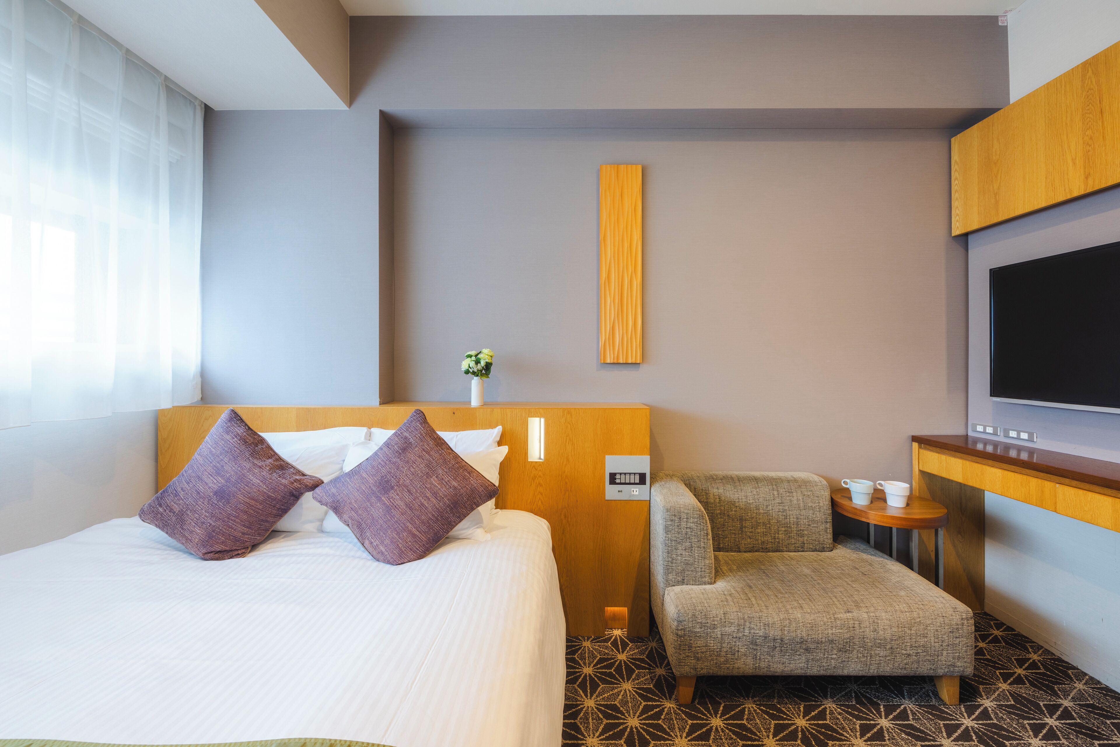 Una habitación de hotel con cama, una silla, un televisor y una mesita.