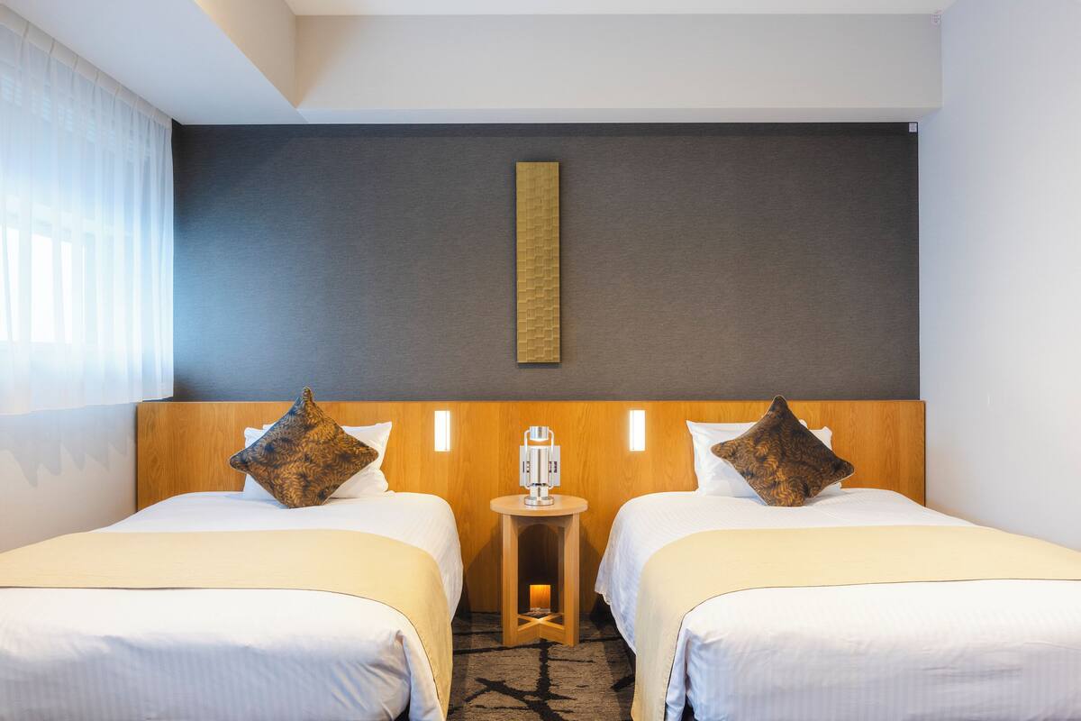 A hotel room with two beds, a small table, and a wall-mounted light fixture.