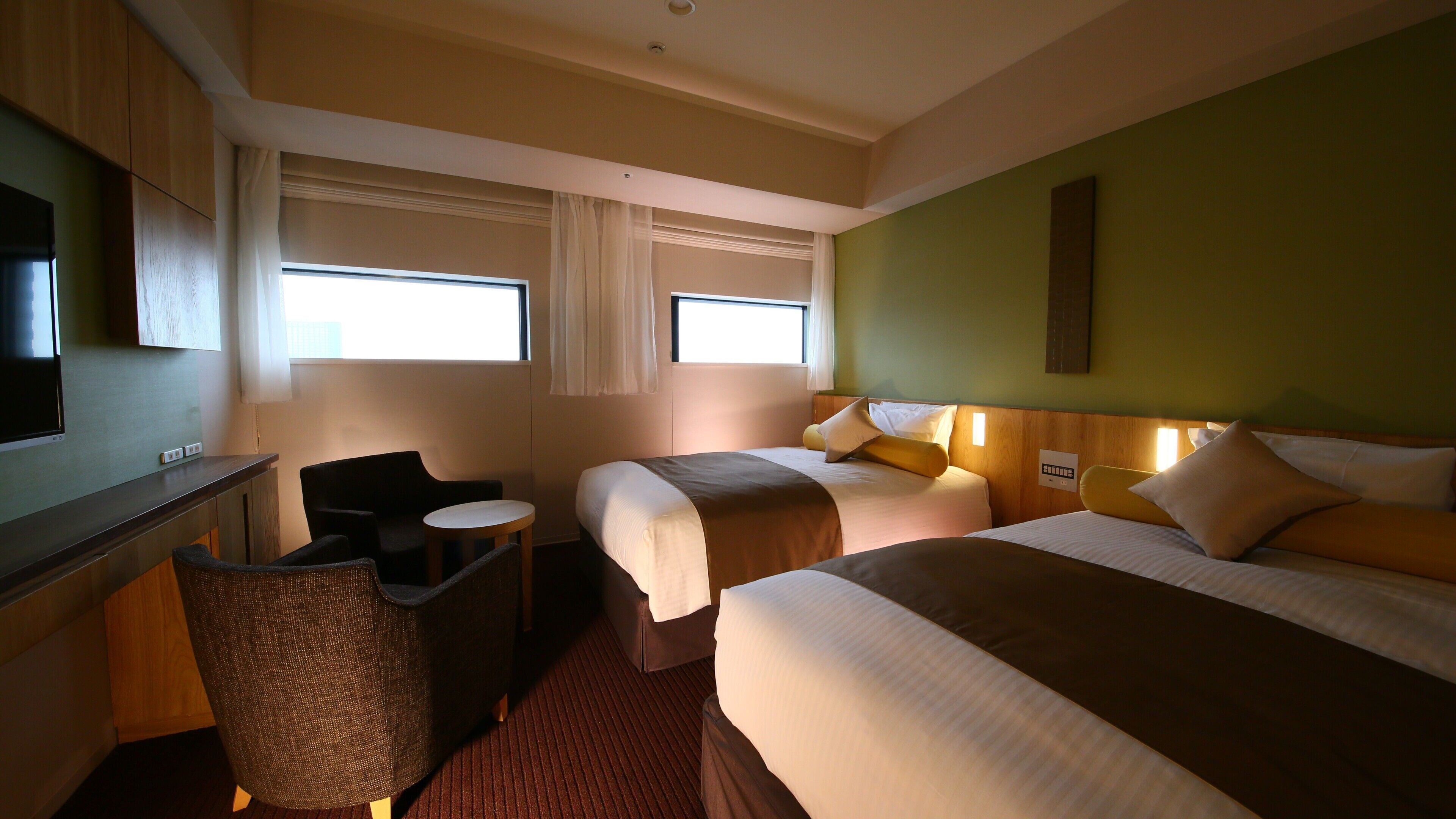 Ein Hotelzimmer mit zwei Betten, einem Schreibtisch, einem Fernseher und einem Sessel.