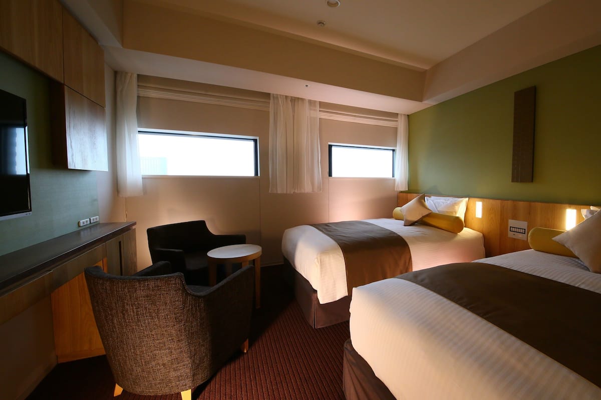 A hotel room with two beds, a desk, a television, and a chair.