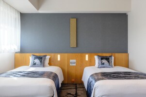 Habitación de hotel con dos camas, cabecero de madera, pared decorativa gris y una lámpara pequeña fijada a la pared.
