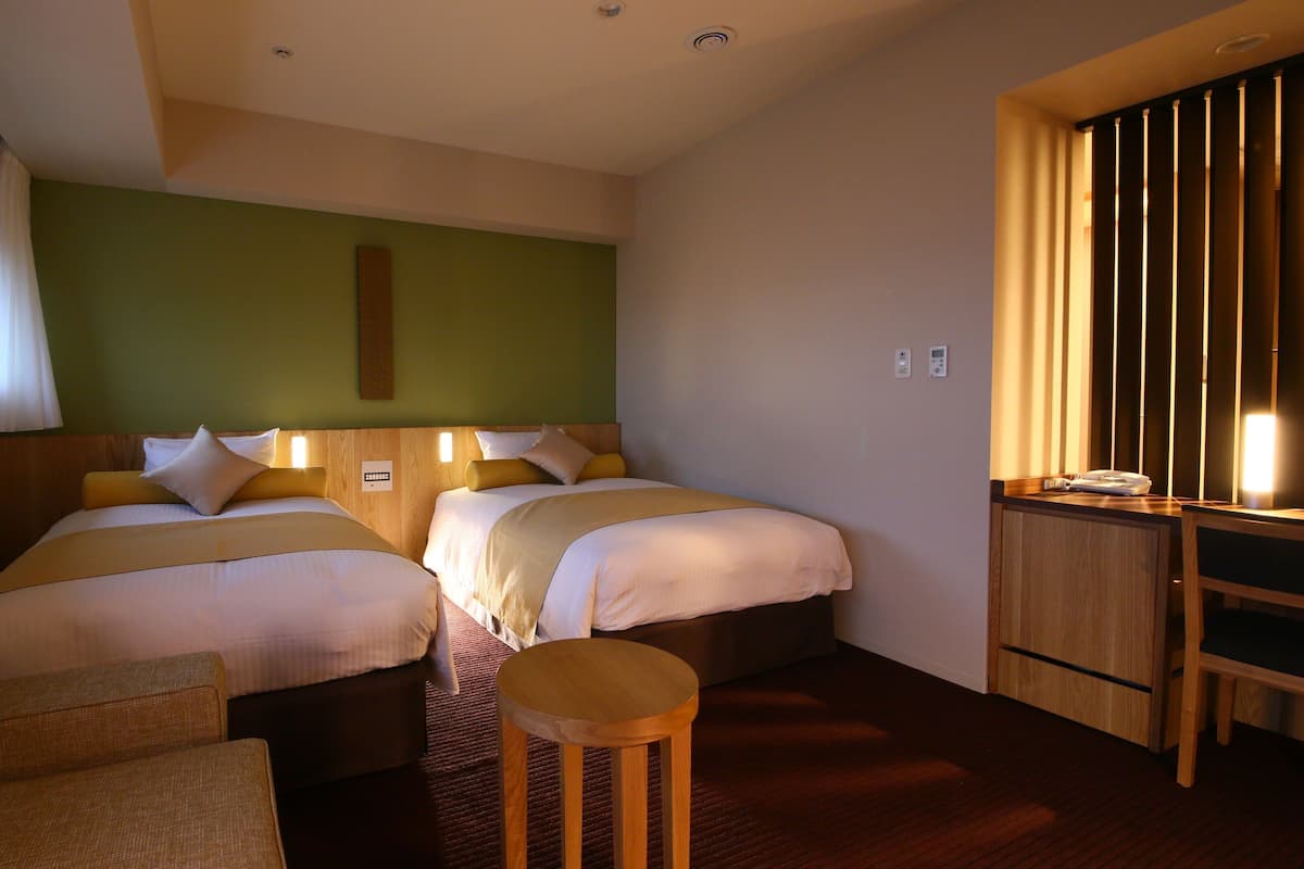 A hotel room with two beds, a desk, a chair, a small table, and a window with curtains.