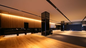 A spacious lobby with wooden flooring, a central seating area, and a modern design with a glass partition.