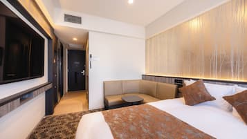 Een hotelkamer met een bed, een zithoek, een televisie en een wandlamp.
