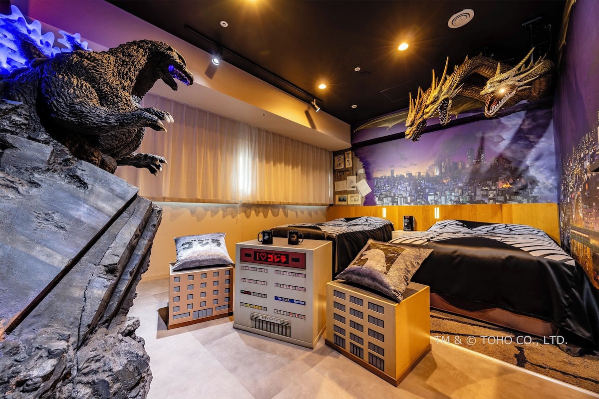 A themed hotel room with a cityscape mural, a large Godzilla statue, and a bed with a city-themed headboard.